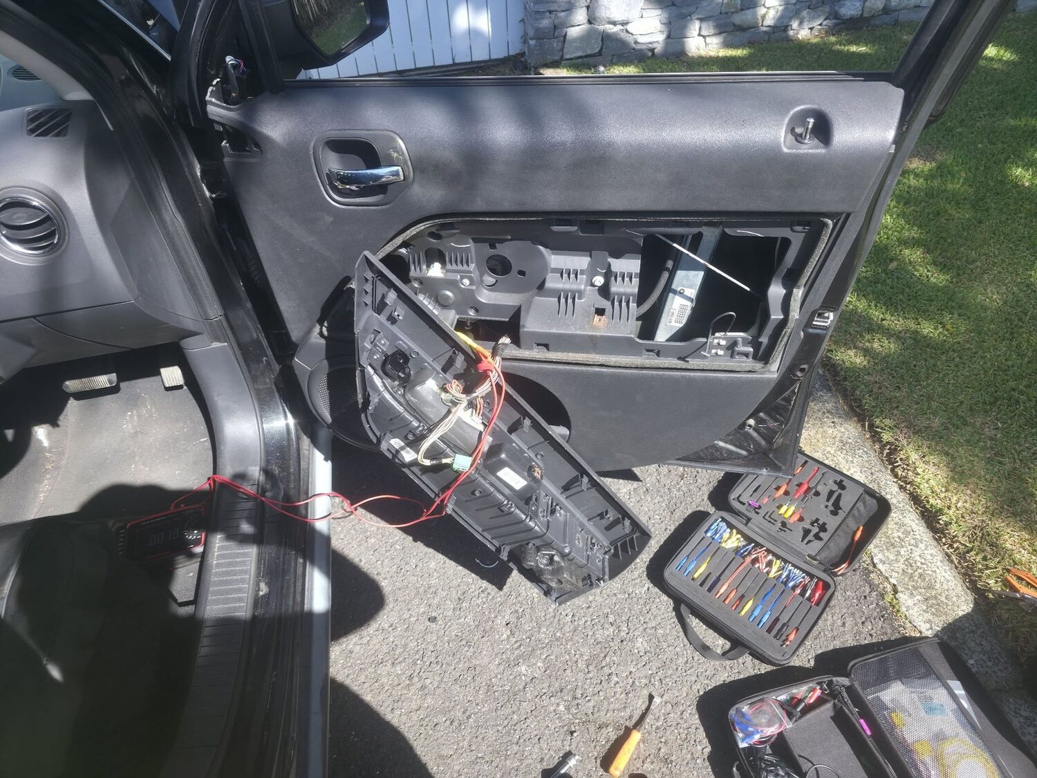 Mobile mechanic working on a European car in a driveway with tools laid out